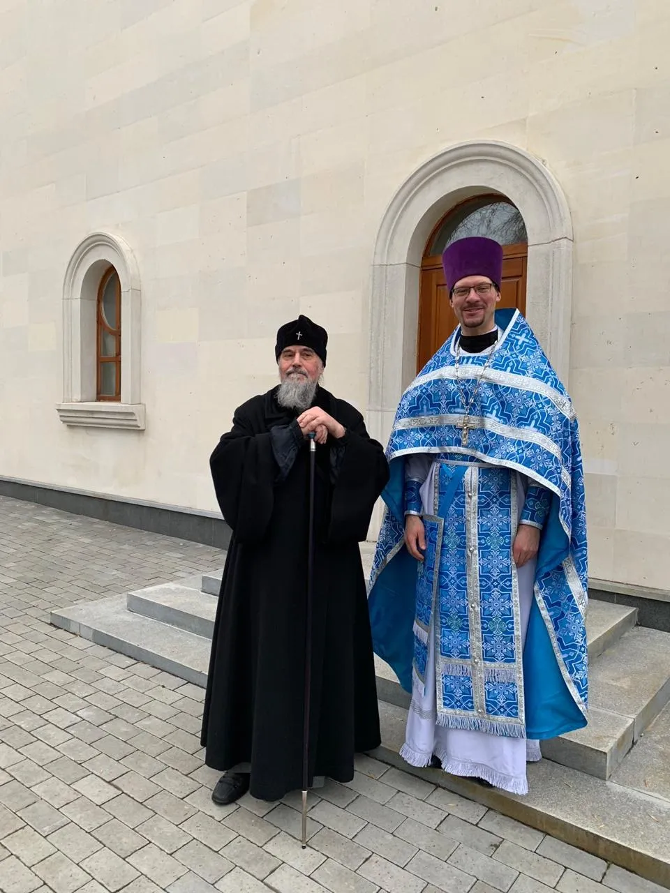 Вход в храм: крыльцо, дверь и арочное окно, у входа два священнослужителя